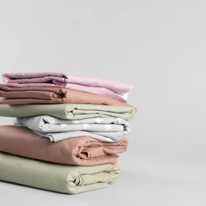 A slightly uneven stack of folded bed sheets that come in a variety of colors with a plain white background.