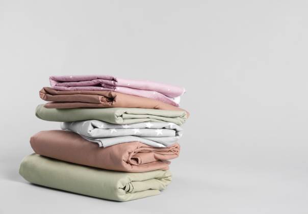 A slightly uneven stack of folded bed sheets that come in a variety of colors with a plain white background.