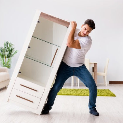 A man trying to drag a shelving unit across the floor. He appears to be rearranging the room he's in.