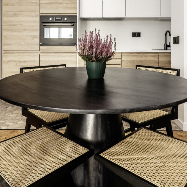 A black dining table surrounded by four chairs. The chairs are also black and have wicker weavings for the seats and backs.
