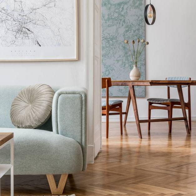 A modern-looking living room with the dining room in the background. The living room has a light teal couch in it.