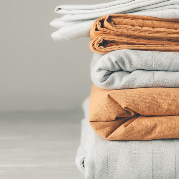 A stack of folded bed sheets sitting on the ground. The sheets in the stack alternate between white and orange.