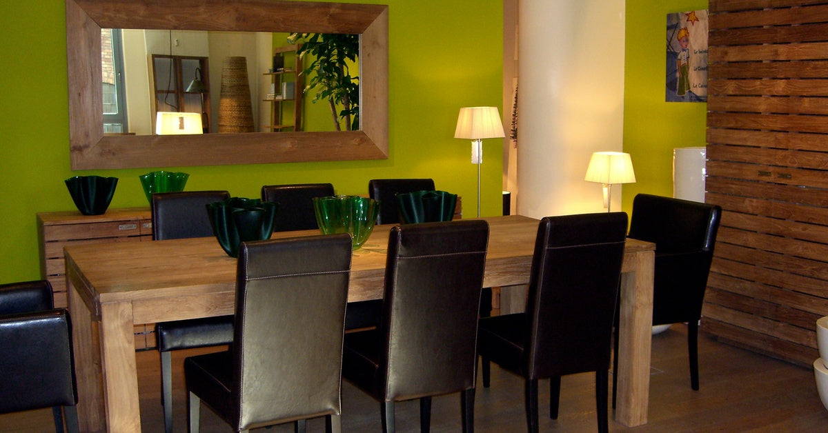 A plain wooden table with eight black chairs surrounding it. There is a mirror on the wall behind the table. 