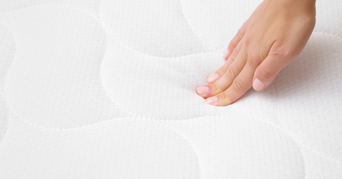 A person, up close and pressing down on a mattress. They only use three fingers to press into the mattress.