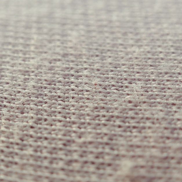 A very close view of some beige bed sheets. You can see the individual fibers and how they're weaved together.