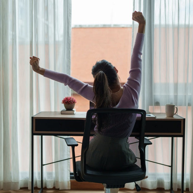 A woman sitting at her desk while stretching and looking out the window. She is using an ergonomic chair.