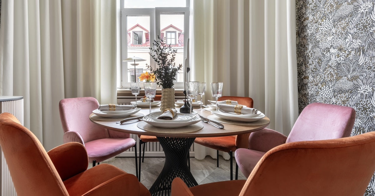 A small dining room table, set with plates, glasses, and silverware. There are five red chairs surrounding the table.