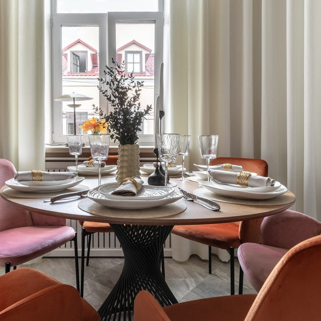 A small dining room table, set with plates, glasses, and silverware. There are five red chairs surrounding the table.