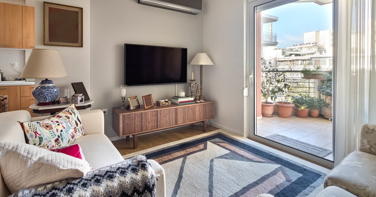 A cramped living room that has two small couches facing a TV. There is also a sliding door that opens up to a balcony.