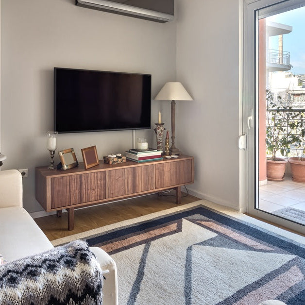 A cramped living room that has two small couches facing a TV. There is also a sliding door that opens up to a balcony.