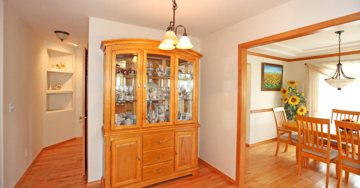 A wooden dining room display cabinet. This one is sitting in the room next to the dining room. The space is very well lit.
