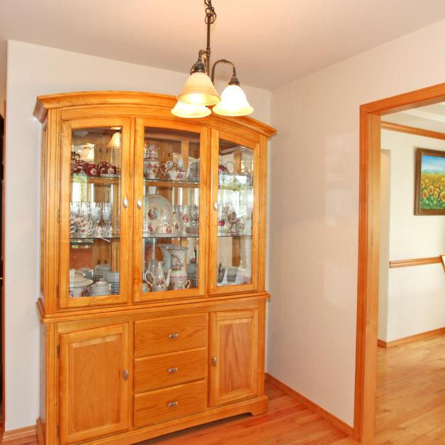 A wooden dining room display cabinet. This one is sitting in the room next to the dining room. The space is very well lit.