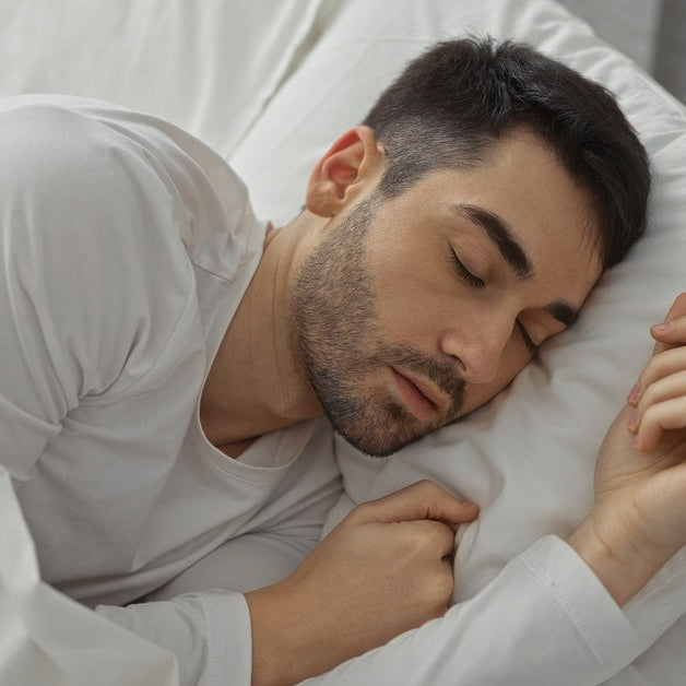 A man sleeping in his bed. He's laying on a pillow and has a white sheet pulled up to his shoulder.
